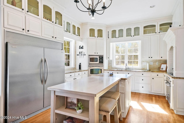 kitchen with light hardwood / wood-style floors, built in appliances, hanging light fixtures, backsplash, and white cabinetry