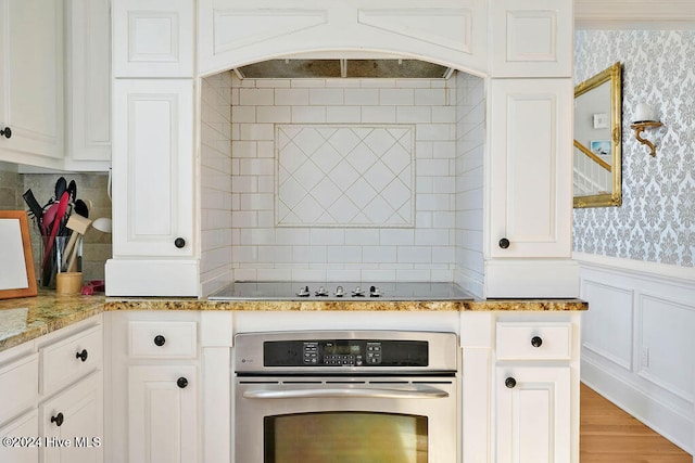 kitchen featuring black electric cooktop, white cabinetry, light stone countertops, hardwood / wood-style floors, and oven