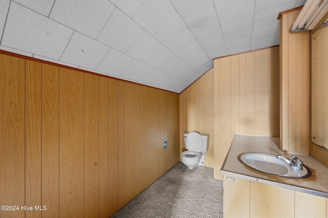 bathroom featuring wood walls, vanity, toilet, and vaulted ceiling