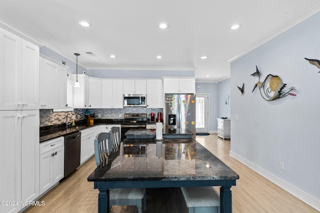 kitchen featuring crown molding, white cabinetry, stainless steel appliances, and hanging light fixtures