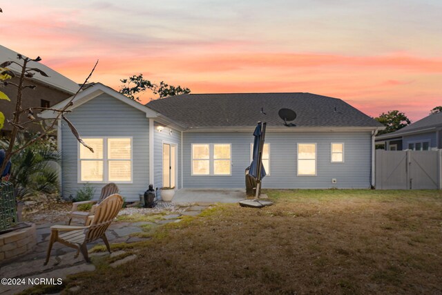 back house at dusk featuring a patio and a lawn