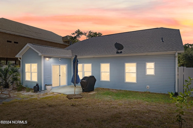 back house at dusk with a patio area and a lawn