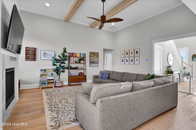 living room with ceiling fan, light hardwood / wood-style flooring, beam ceiling, and a fireplace