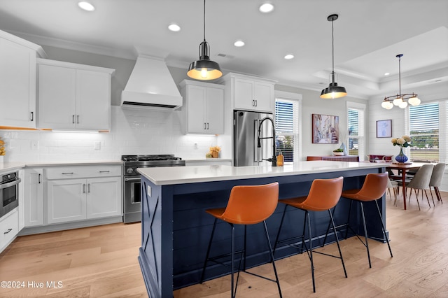 kitchen featuring high quality appliances, premium range hood, white cabinetry, and a center island with sink