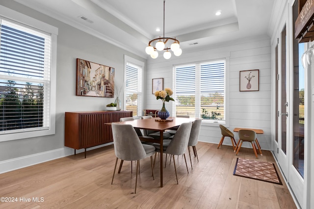 dining area with light hardwood / wood-style floors, crown molding, a tray ceiling, and wood walls