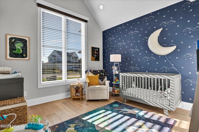 bedroom with vaulted ceiling, hardwood / wood-style floors, and a crib