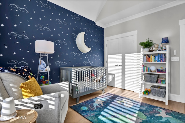 bedroom featuring lofted ceiling, a nursery area, crown molding, and hardwood / wood-style floors