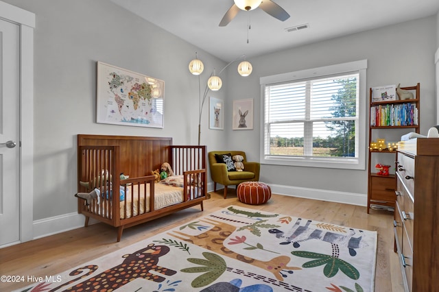 bedroom featuring ceiling fan, light hardwood / wood-style flooring, and a crib