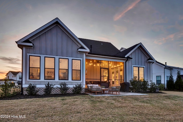 back house at dusk with an outdoor hangout area, a patio area, and a yard