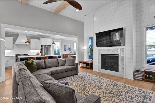 living room featuring light hardwood / wood-style floors, ceiling fan, beamed ceiling, and a fireplace