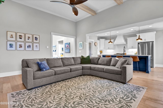 living room with ceiling fan, a high ceiling, beam ceiling, and light wood-type flooring