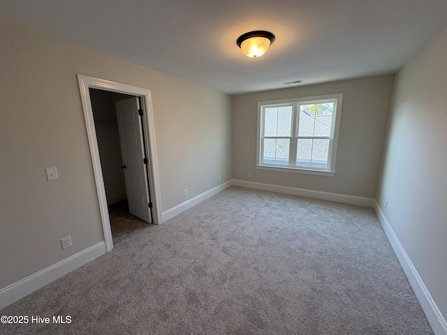 unfurnished bedroom featuring carpet floors, a walk in closet, visible vents, and baseboards