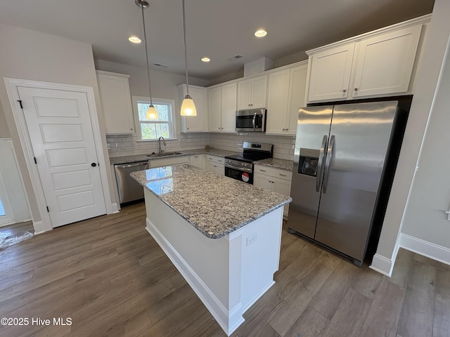 kitchen with dark wood-style flooring, appliances with stainless steel finishes, white cabinetry, a sink, and a kitchen island