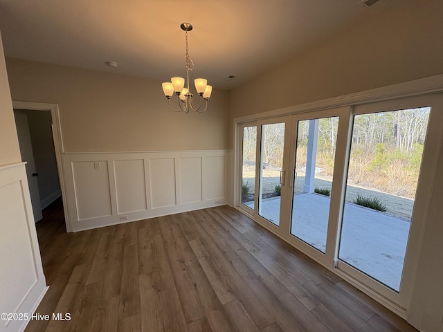 unfurnished dining area with a chandelier, french doors, a wainscoted wall, and wood finished floors