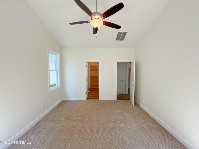 unfurnished bedroom with a closet, a spacious closet, vaulted ceiling, light colored carpet, and ceiling fan