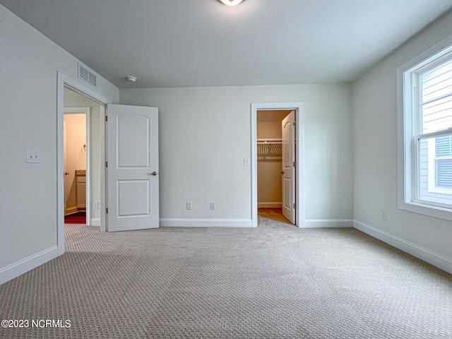 unfurnished bedroom featuring light colored carpet, a spacious closet, and a closet