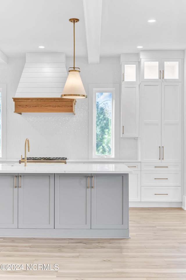 kitchen featuring premium range hood, white cabinetry, light wood-type flooring, beamed ceiling, and decorative light fixtures