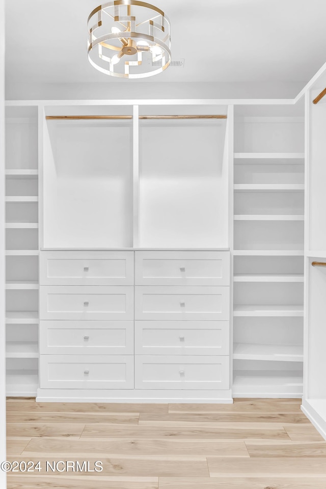 walk in closet with light hardwood / wood-style flooring and an inviting chandelier