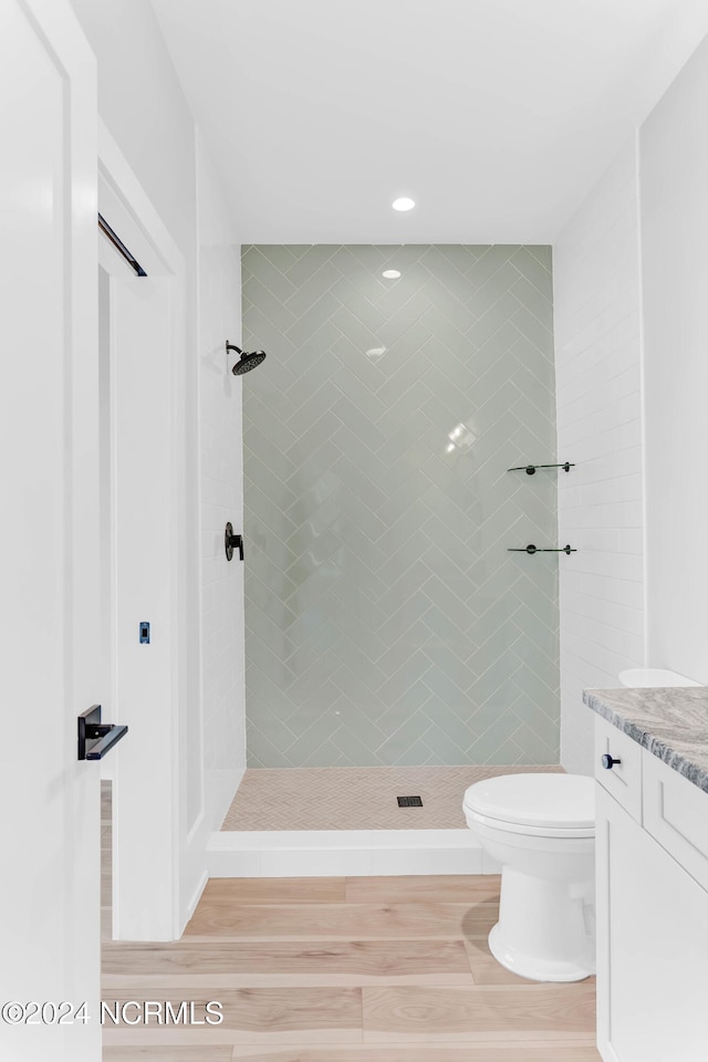 bathroom with toilet, hardwood / wood-style floors, vanity, and tiled shower