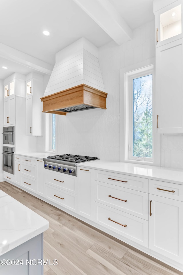 kitchen featuring appliances with stainless steel finishes, beamed ceiling, white cabinets, custom range hood, and light hardwood / wood-style flooring