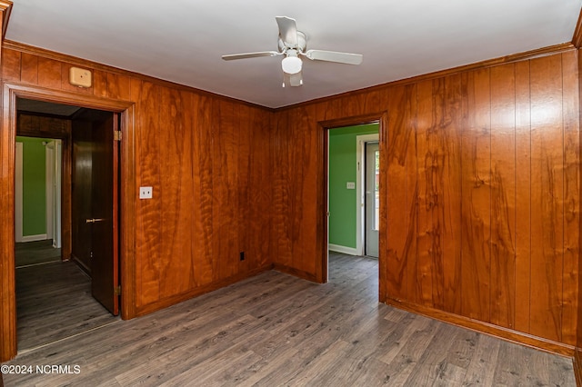 empty room with ornamental molding, ceiling fan, wooden walls, and dark hardwood / wood-style flooring