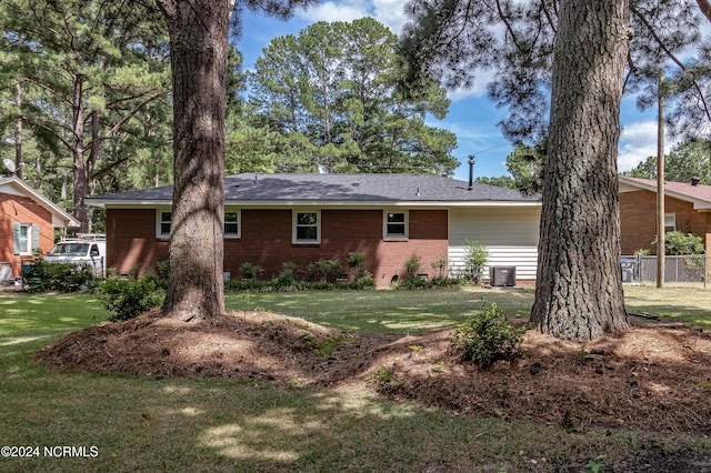 rear view of property with central air condition unit and a lawn