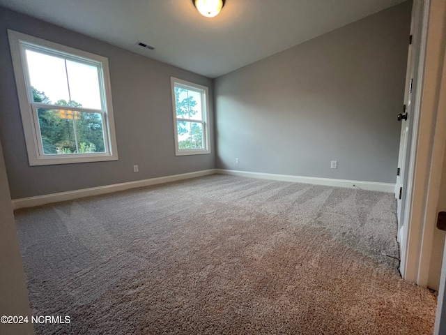 carpeted empty room with lofted ceiling, baseboards, and visible vents