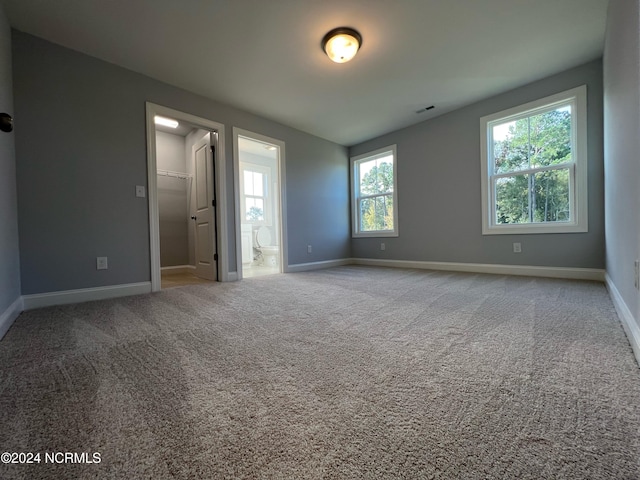 unfurnished bedroom with carpet floors, a walk in closet, visible vents, connected bathroom, and baseboards