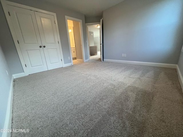 unfurnished bedroom with carpet, a closet, ensuite bath, and baseboards