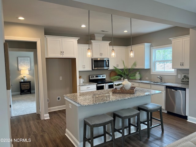 kitchen featuring dark wood finished floors, stainless steel appliances, white cabinets, a sink, and a kitchen island