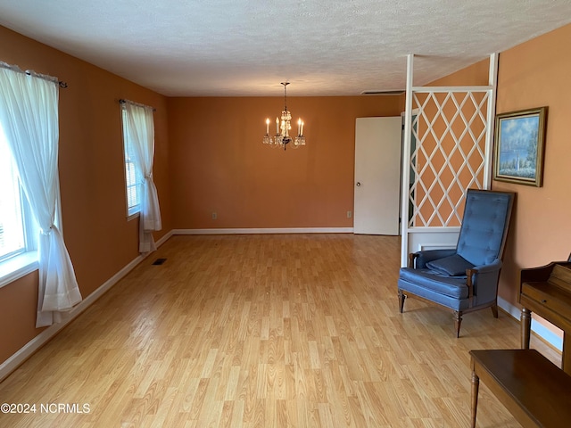 unfurnished room with a textured ceiling, light hardwood / wood-style flooring, and a notable chandelier