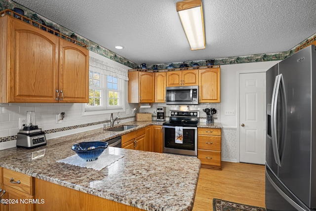 kitchen featuring sink, light stone counters, kitchen peninsula, a textured ceiling, and appliances with stainless steel finishes