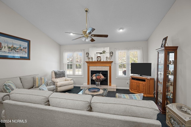 living room with ceiling fan, plenty of natural light, a tile fireplace, and vaulted ceiling