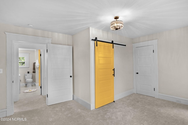 unfurnished bedroom with a barn door, light carpet, and ensuite bathroom
