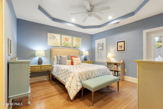 bedroom featuring light hardwood / wood-style floors, a raised ceiling, and ceiling fan