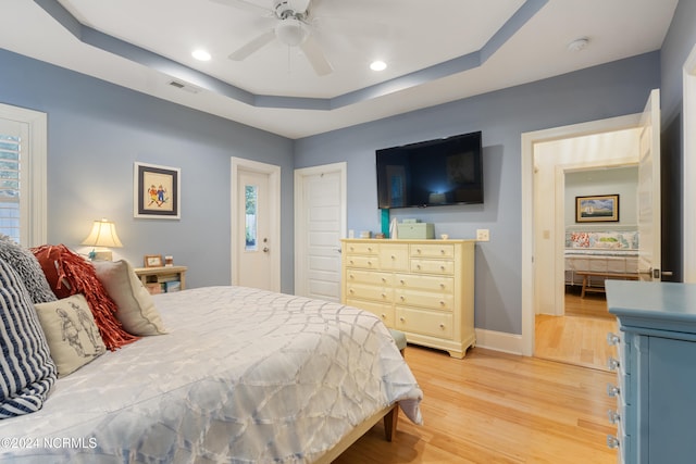 bedroom featuring ceiling fan, a tray ceiling, and light hardwood / wood-style flooring