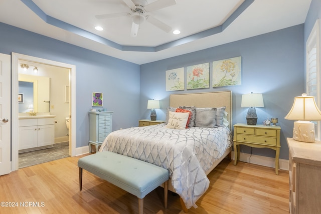 bedroom with a raised ceiling, light wood-type flooring, and ceiling fan