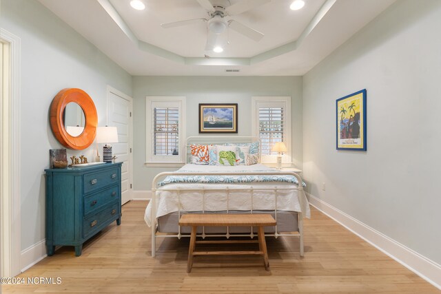 bedroom featuring light hardwood / wood-style flooring, a raised ceiling, and ceiling fan