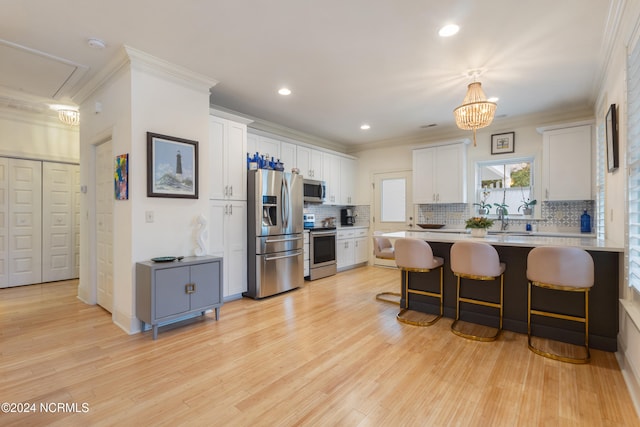 kitchen featuring light hardwood / wood-style flooring, a breakfast bar, crown molding, white cabinets, and appliances with stainless steel finishes