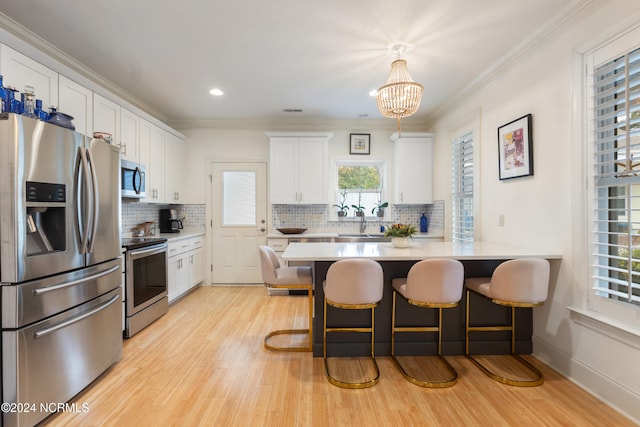 kitchen with a breakfast bar area, stainless steel appliances, pendant lighting, light wood-type flooring, and white cabinetry