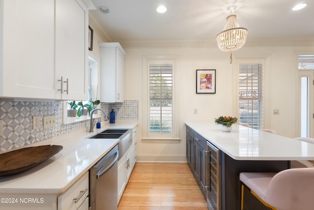 kitchen featuring light wood-type flooring, hanging light fixtures, white cabinetry, stainless steel dishwasher, and ornamental molding