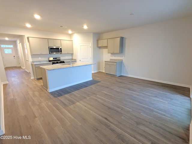 kitchen featuring appliances with stainless steel finishes, light hardwood / wood-style floors, sink, gray cabinets, and a kitchen island with sink