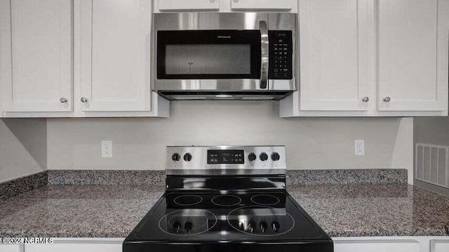 kitchen with white cabinetry, stainless steel appliances, and dark stone counters