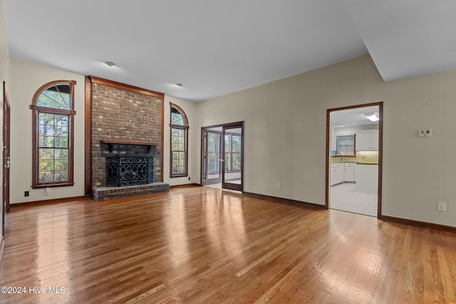 unfurnished living room featuring light wood-type flooring and a brick fireplace