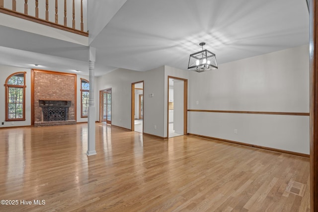 unfurnished living room featuring ornate columns, light wood-type flooring, a notable chandelier, and a brick fireplace