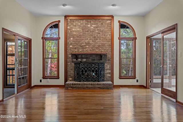 unfurnished living room featuring a fireplace, wood-type flooring, french doors, and a wealth of natural light