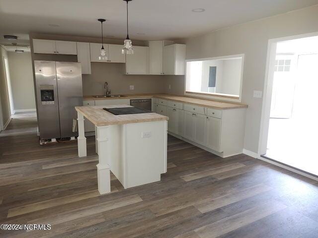 kitchen with hanging light fixtures, stainless steel refrigerator with ice dispenser, sink, a center island, and white cabinets