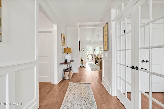 hallway featuring light hardwood / wood-style flooring, french doors, beam ceiling, and crown molding