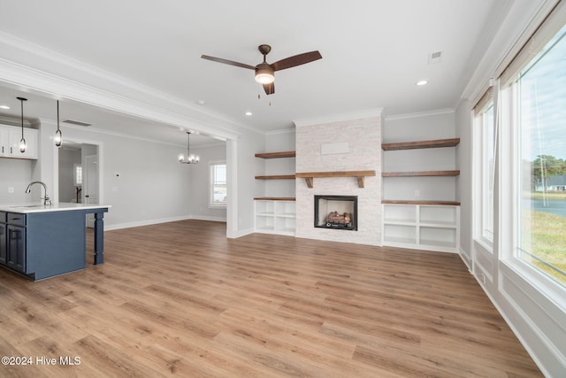 unfurnished living room featuring a stone fireplace, light wood-type flooring, a healthy amount of sunlight, and sink