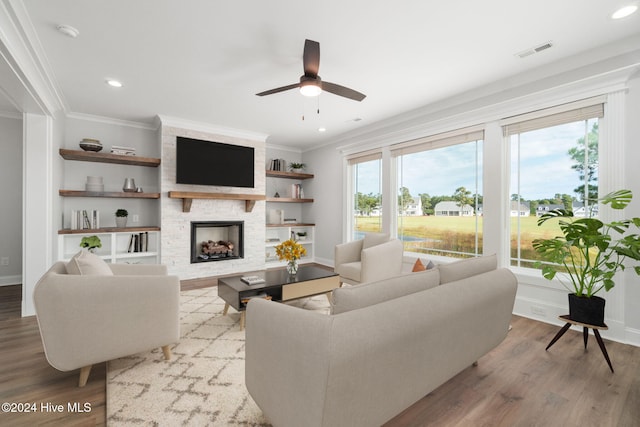 living room featuring crown molding, light hardwood / wood-style flooring, a stone fireplace, and ceiling fan